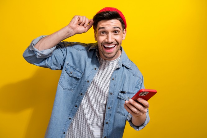 Photo of positive funky guy wear denim jacket chatting apple iphone samsung modern device isolated yellow color background.