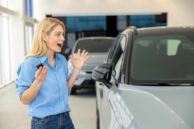 Feeling happy. Pretty long-haired blonde woman near a new car looking enjoyed and excited